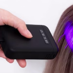 A handheld black V-Light UV curing device being used to bond specialized hair extensions with precision light technology.